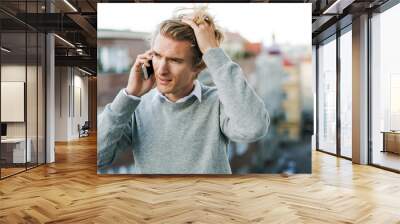 Young man with smartphone standing on a balcony in city, making a phone call. Wall mural