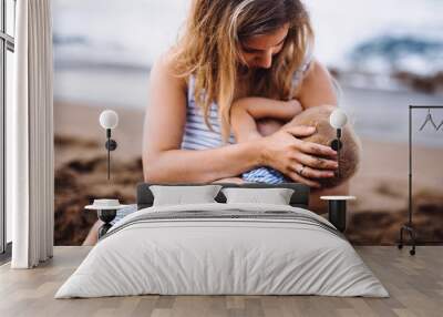 Young mother breasfeeding toddler daughter on beach on summer holiday. Wall mural