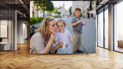 Young mother playing with her kids, blowing bubbles in city street in summer. Wall mural