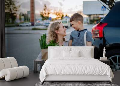 Young mother with little son after shopping holding zero waste shopping bags with grocery near car. Wall mural