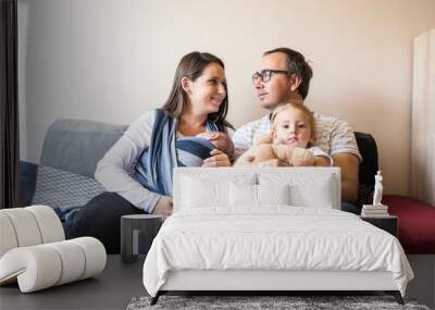 Young parents with children sittin on sofa, baby sling Wall mural