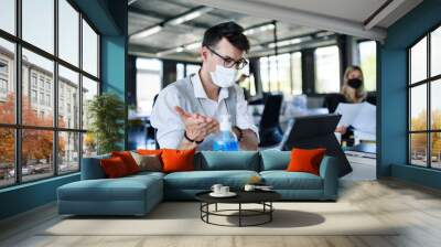 Young people with face masks back at work in office after lockdown, disinfecting hands. Wall mural