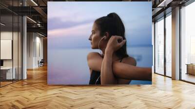 Young sportive girl stretching in the morning and listening music, outdoor near the lake. Wall mural