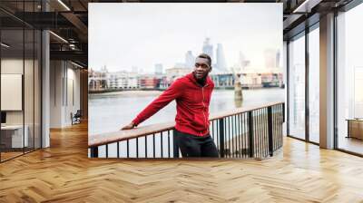 Young sporty black man runner on the bridge outside in a city, resting. Wall mural