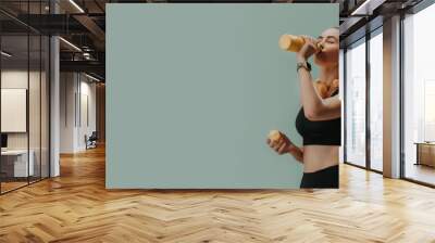 Young sporty woman in sportswear with wireless headset drinking from bottle over green background, copy space Wall mural