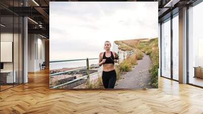 Young sporty woman runner with earphones running by sea in nature. Wall mural