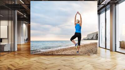 Young sporty woman runner with earphones stretching on the beach outside. Wall mural