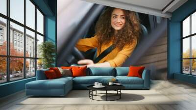 Young woman driving a car in the city. Portrait of a beautiful woman in a car, looking out of the window and smiling. Wall mural