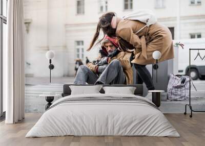 Young woman giving money to homeless beggar man sitting in city. Wall mural