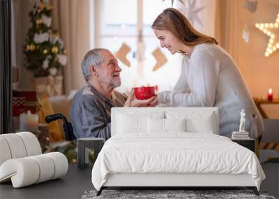 Young woman giving tea to senior grandfather in wheelchair indoors at home at Christmas. Wall mural