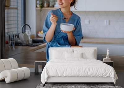 Young woman having muesli for breakfast in her kitchen, morning routine and healthy lifestyle concept. Wall mural