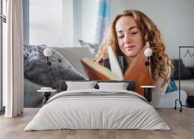 Young woman relaxing indoors at home with book. Wall mural