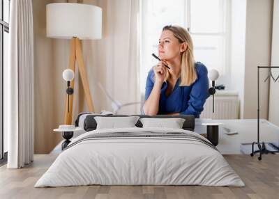 Young woman sitting at the desk indoors in home office, working. Wall mural