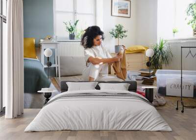 Young woman sorting wardrobe indoors at home, charity donation concept. Wall mural