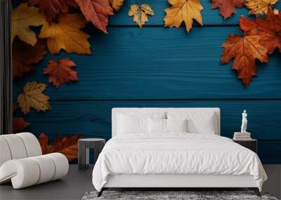 Red and orange maple leaves on a blue wooden table with a wooden background and frame made of autumn foliage. Wall mural