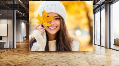 Young woman holding colorful autumn leaves in her warm hat and smiling in an outdoor lifestyle photo Wall mural