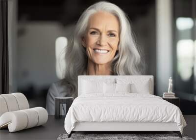 A portrait of an elegant middle-aged woman with long silver hair, smiling warmly at the camera in her modern office space.
 Wall mural