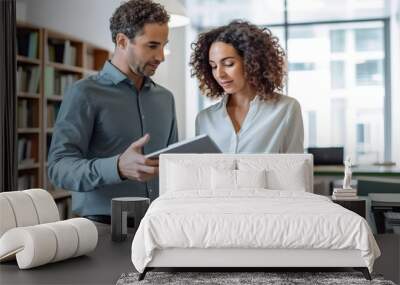 portrait of a male and female professional in their late thirties, dressed in casual business attire, engaged in a discussion over a tablet screen together in an office setting.  Wall mural