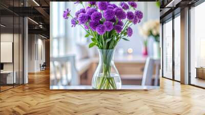 Close up purple flowers in single clear glasses decorate a white dining table. The background is blurred, leaving space for text. Wall mural