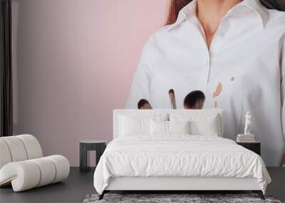 Spilling foundation on a woman's white shirt, in the hands makeup brushes, isolated on pink background. space for text Wall mural