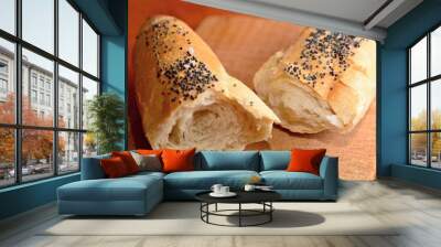 Two pieces of a white bread roll sprinkled with poppy seed and salt on a wooden cutting board. Wall mural