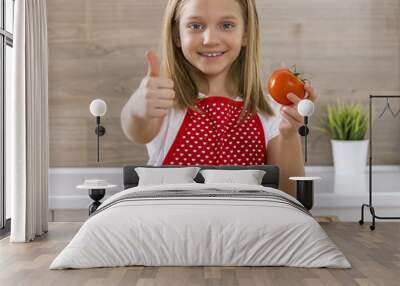 Beautiful little girl cooking in the kitchen and showing thumbs. Wall mural