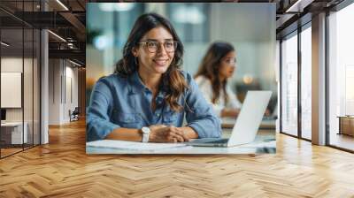 Professional young woman smiling while working on a laptop in a modern office environment Wall mural