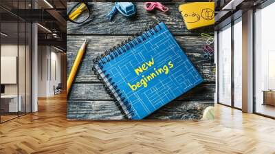 A blue notebook with the words New Beginnings written on it, surrounded by various office supplies on a wooden table Wall mural