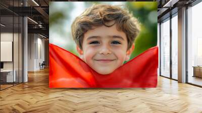 A young boy joyfully holds up a vibrant red cloth outdoors in a lush green setting during a bright sunny day Wall mural