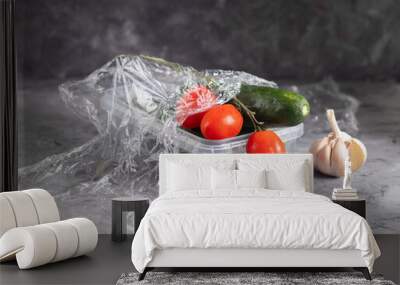 Tomatoes and cucumbers in a transparent plastic bag with cling film and garlic on a light background Wall mural