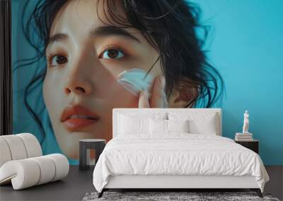 portrait of a korean woman applying face cream skin care product, blue background Wall mural