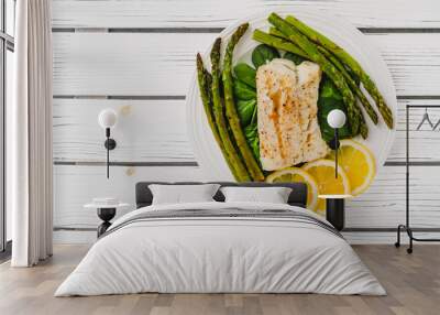 Cod fillet baked with garlic butter sauce served with fresh spinach and roasted asparagus on a white plate close-up Wall mural