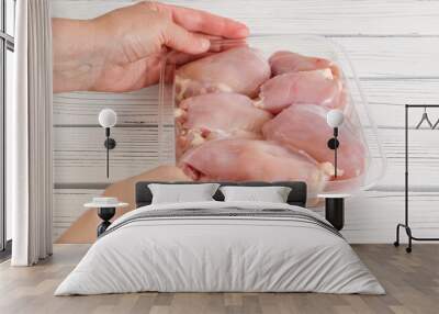 Raw chicken thighs in plastic container in woman's hands close-up on white wooden background Wall mural