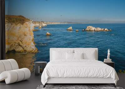 Rocky cliffs and scattered sea stacks along a clear, blue coastline. Wall mural