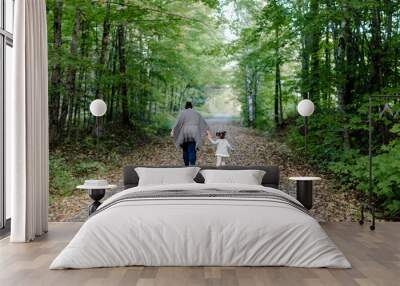 Back view of a mother with her daughter walking on a pathway covered in autumn foliage in a park Wall mural