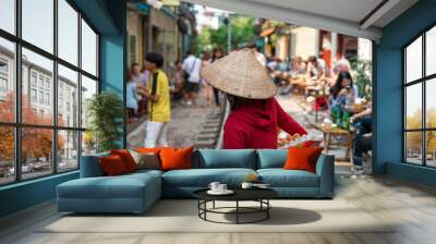 Vietnamese woman vendor walking along railroad with people drink coffee or walking on railways waiting for train to arrive on railway road in Hanoi, Vietnam. Wall mural