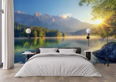 A tranquil lake reflects mountains as the sun rises behind trees in a serene morning landscape Wall mural