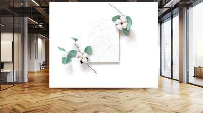 Flower composition. Eucalyptus branches with round leaves, cotton flowers are on a white background. A sheet of paper with a marble pattern is in the center of the layout. Flat lay. Copy space. Wall mural