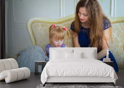 Young mother and her baby daughter looking photobook togerher at home. Family, childhood and leisure concept Wall mural