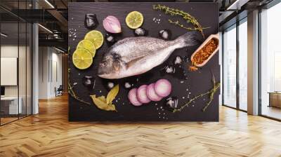 Fresh raw dorada fish with lime, red onion, spices and herbs over black stone background. Selective focus. Top view Wall mural