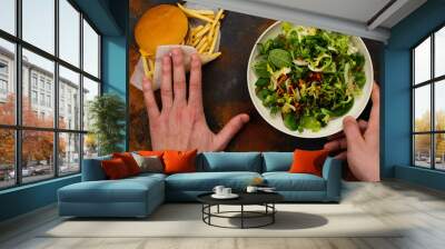 Young man making choice between healthy salad and fast food. Choosing healthy meal instead of burger. Diet or healthy lifestyle concept Wall mural