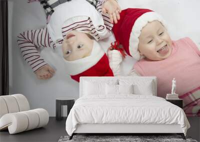 Two children in red Christmas caps are lying on white background Wall mural