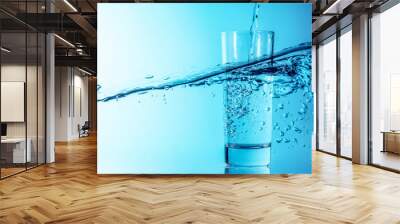 Blue water splash pours into a glass on a beautiful blue sea wave background. Glass of clean drinking blue water with bubbles. Wall mural