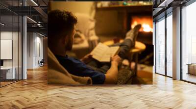 A man is reading a book in front of a hot fireplace. Cozy winter atmosphere Wall mural