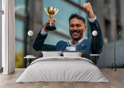 A triumphant businessman in a suit holds a golden trophy aloft, symbolizing his success and recognition as a top-performing employee Wall mural