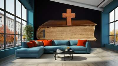 Wooden cross on closed old bible, dark backdrop. Christian faith, religion, culture. Prayer seeking Wall mural