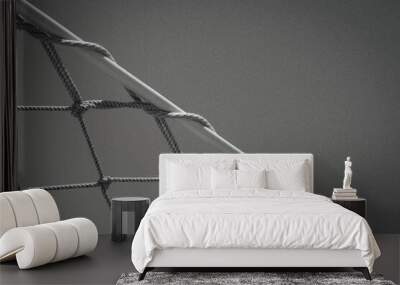 black and white image shows a close-up of a rope net, possibly part of a playground or a ship, against a smooth background. The net’s ropes are taut and intersecting at knots. Wall mural