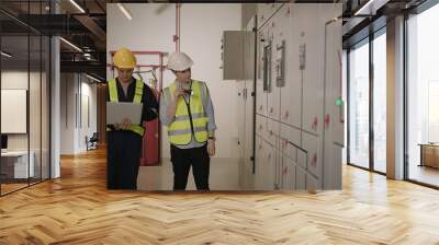 Two electricians electrical engineers in protective uniform checking voltage control panel screen system at electrical cabinet for generate electricity of factory in manufacture industrial Wall mural