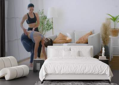 Two women in activewear performing Practicing yoga poses Together in a bright modern living room with natural light and indoor plants. Wall mural