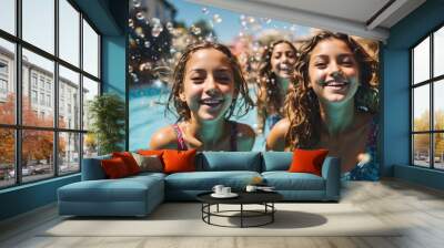 Snapshot of girls in high spirits, smiling and making eye contact with the camera as they swim in a sparkling blue pool with bubbles on a sunny day. Wall mural